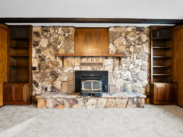 Stone fireplace with wood-burning insert, flanked by built-in shelving and lower cabinetry