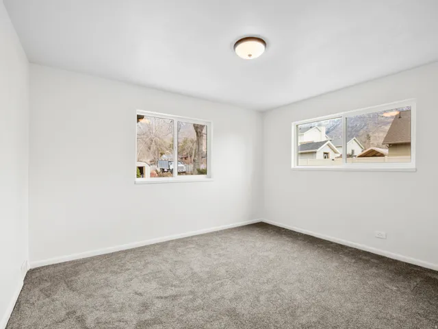 Neutral wall color with two windows, plush gray carpeting, and a flush-mount ceiling light fixture