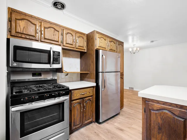 Kitchen featuring stainless steel appliances, wood-finish cabinetry, light countertops, and wood-finish flooring