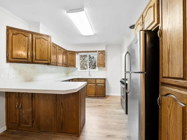 U-shaped kitchen featuring wood cabinetry, white countertops, tile backsplash, and wood-finish flooring