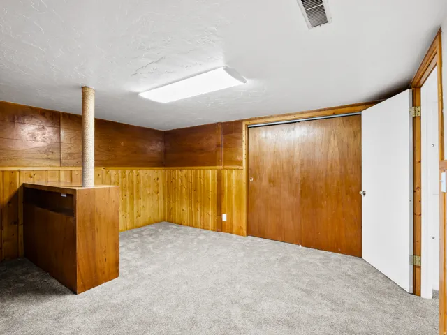 Carpeted room featuring wood paneling, a built-in wood-finish bar, and a bi-fold closet door with wood-finish panels