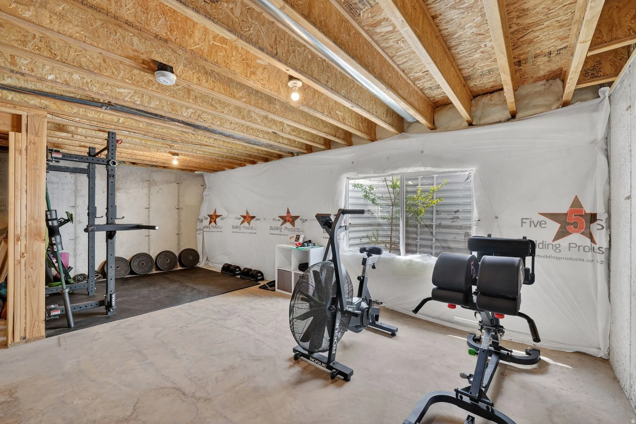 Unfinished basement space featuring exposed wood joists, concrete flooring, and an egress window
