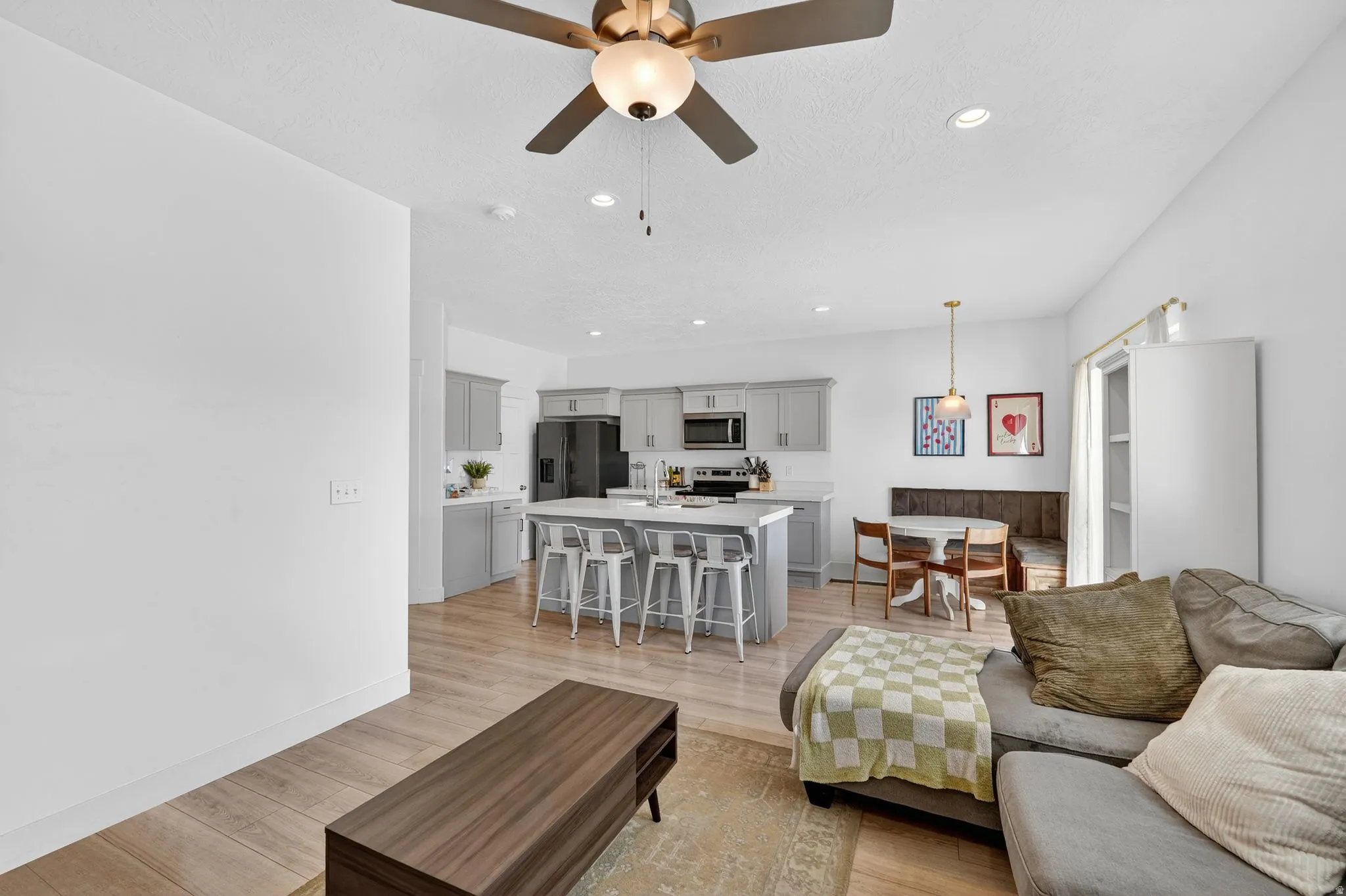 Open-concept living area featuring wood-finish flooring, a contemporary ceiling fan with light, recessed lighting, and a neutral color palette