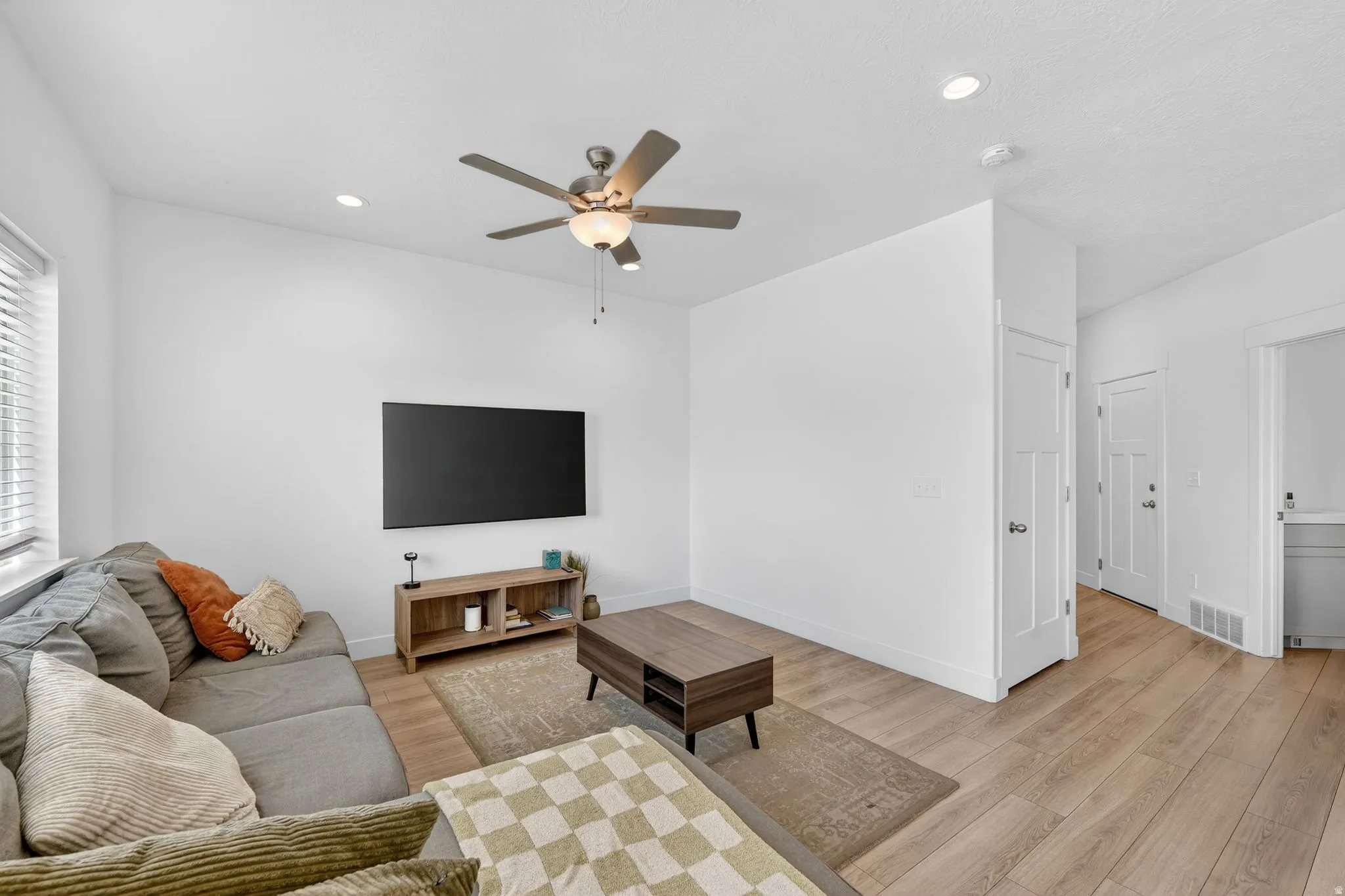 Bright living area featuring wood-finish flooring, recessed lighting, a ceiling fan with integrated light fixture, a window with blinds, and white interior doors