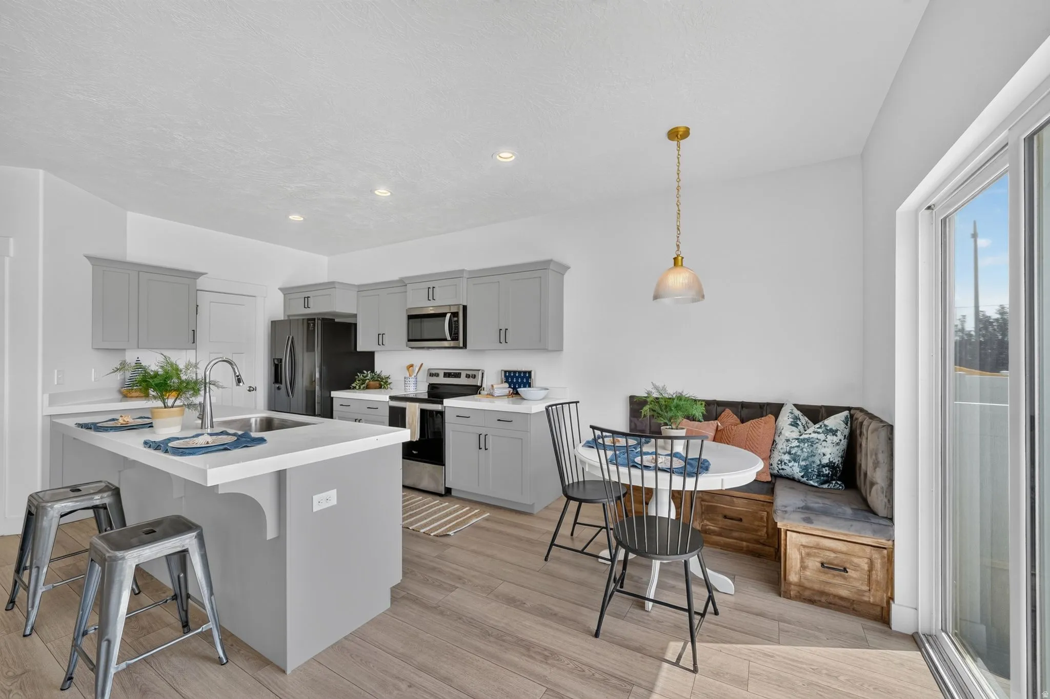 Modern kitchen featuring light gray cabinetry, stainless steel appliances, a center island with sink, wood-finish flooring, and a sliding glass door