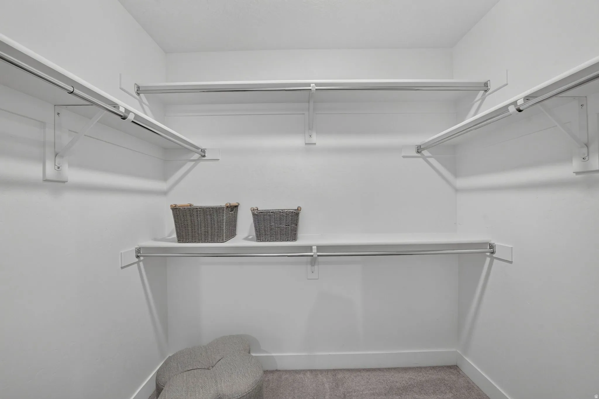 Walk-in closet featuring white wire shelving, hanging rods, and light gray carpeting