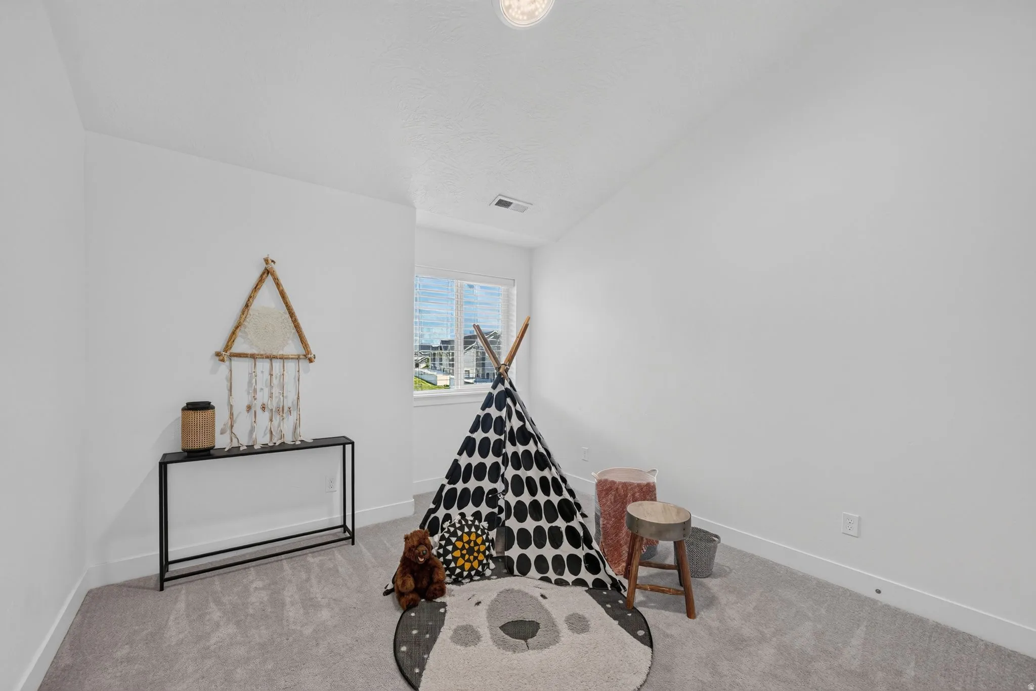 Bright interior space featuring light gray carpeting, crisp white walls, a large window, a ceiling-mounted light fixture, and white baseboards