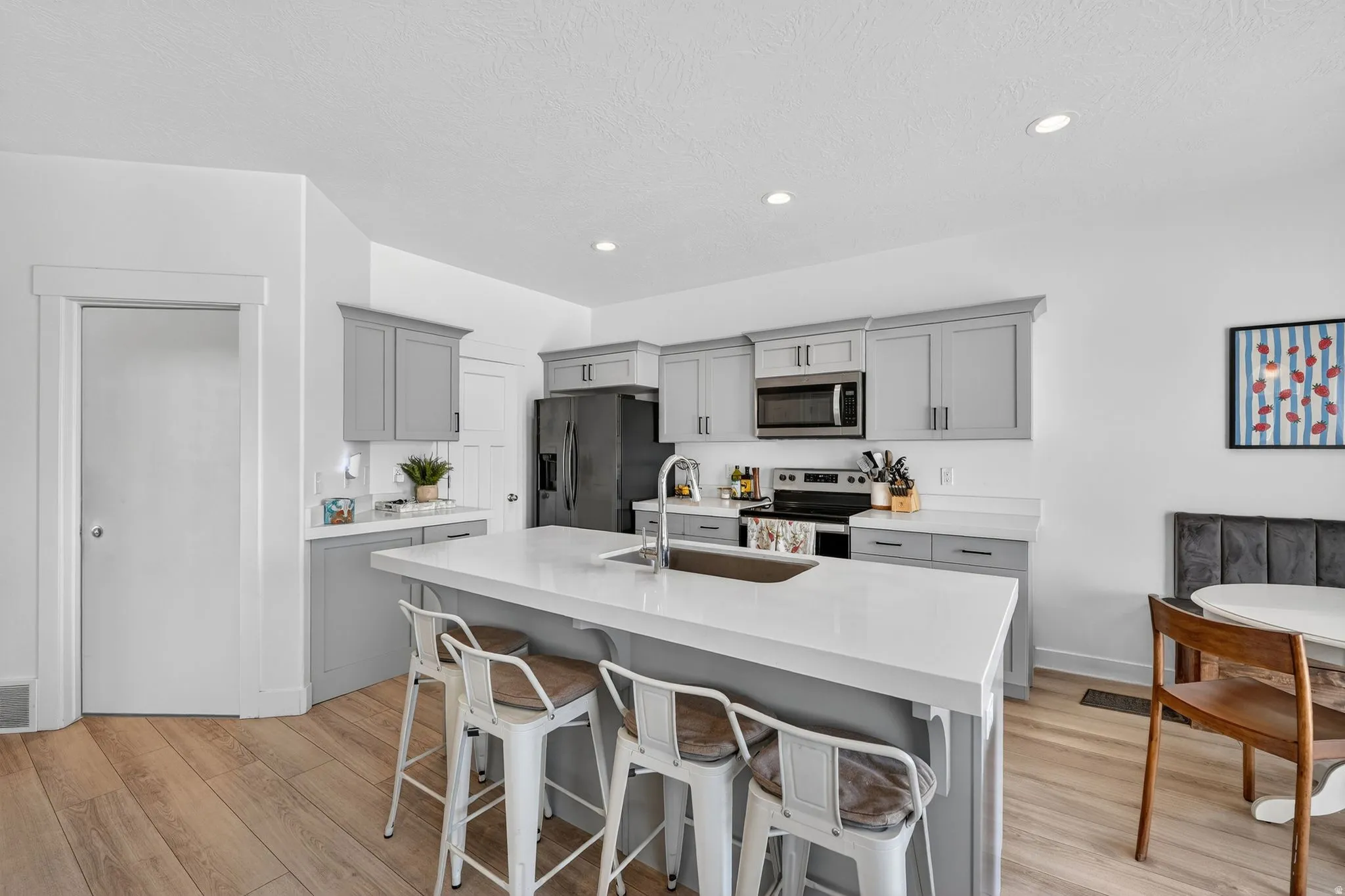 Open-concept kitchen featuring an island with seating, gray cabinetry, quartz countertops, stainless steel appliances, and wood-finish flooring