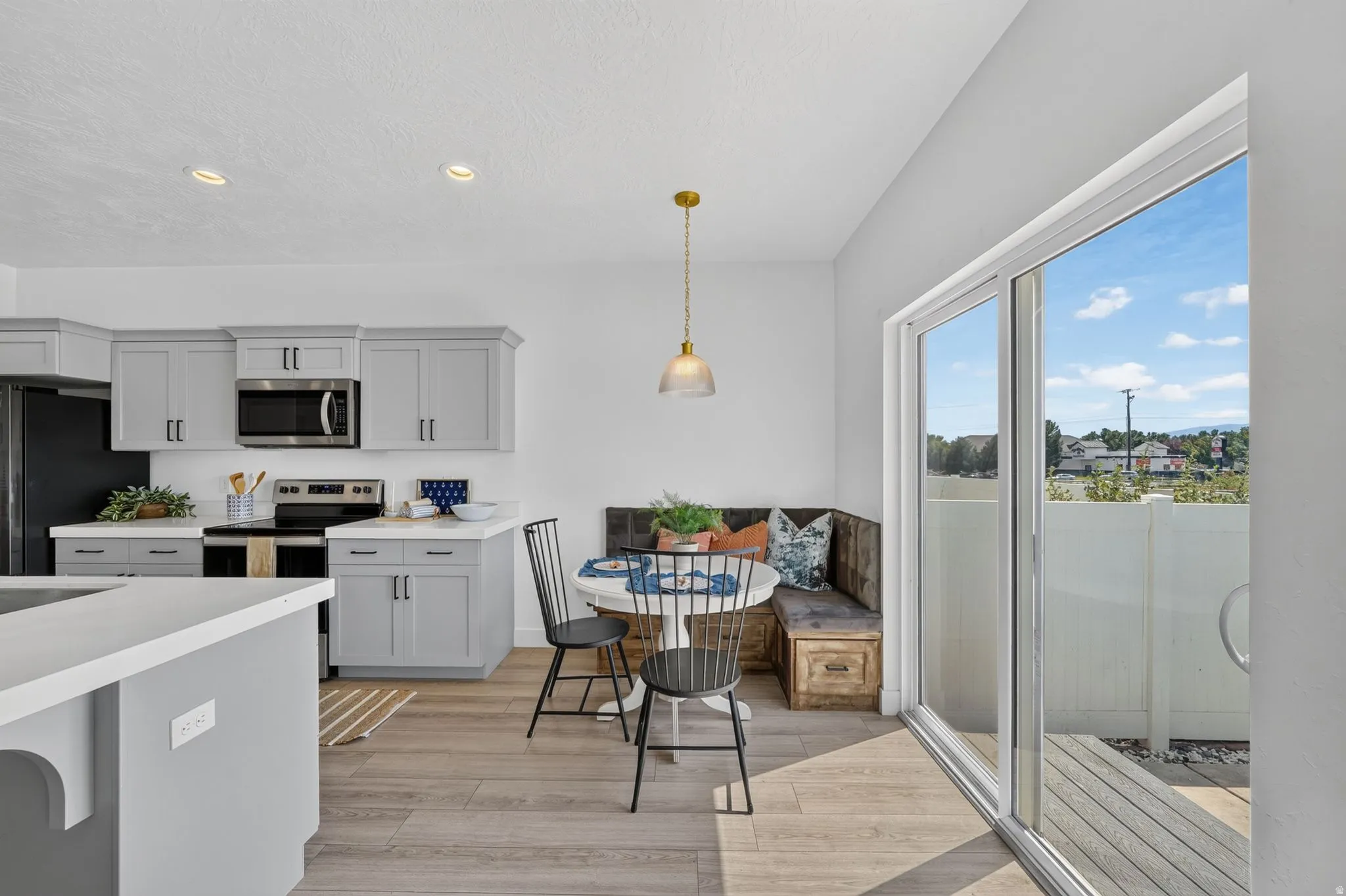 Open-concept kitchen and dining area featuring light gray cabinetry with dark hardware, stainless steel appliances, and light-toned countertops
