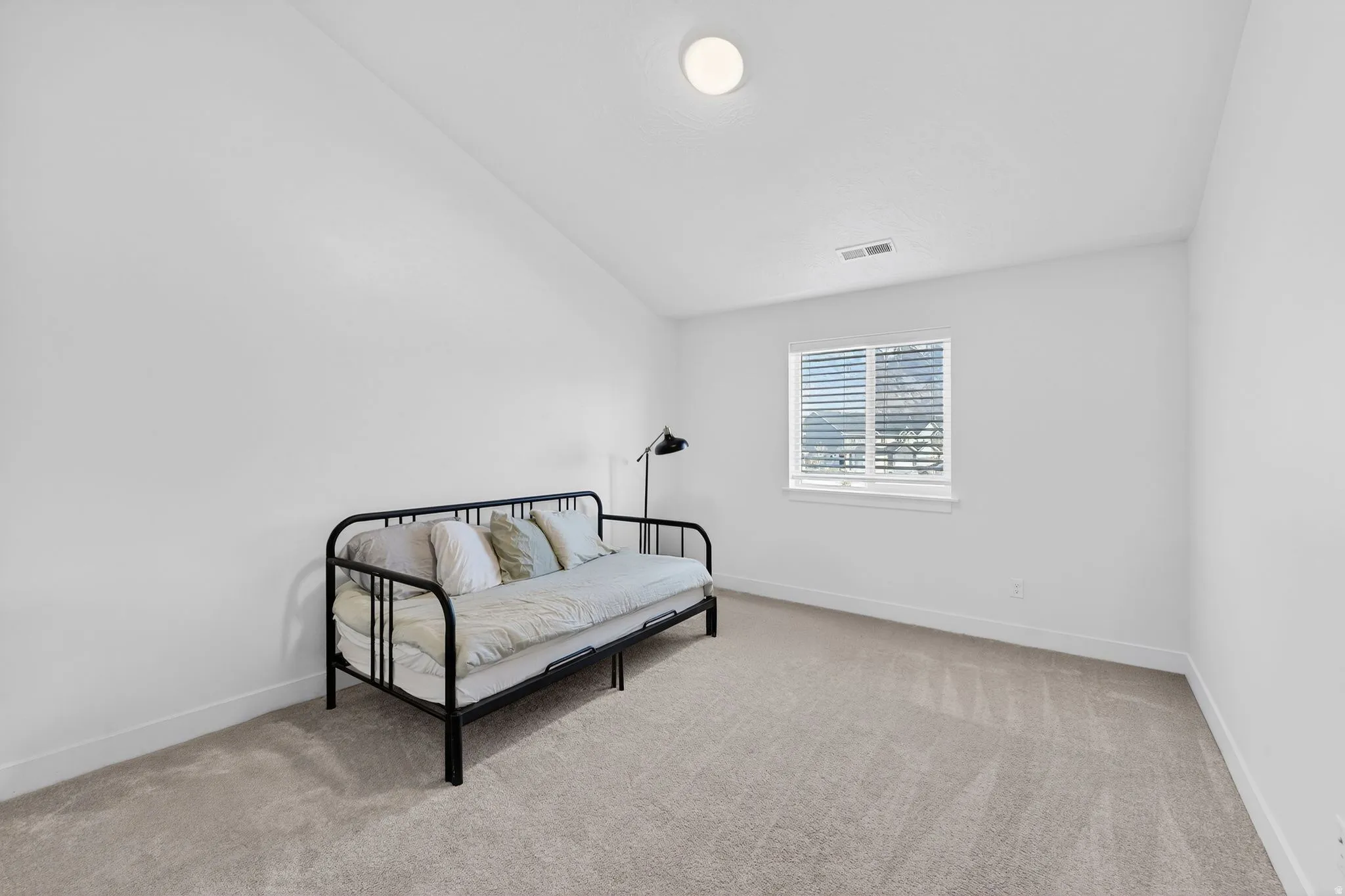 Bright interior room featuring a window with horizontal blinds, neutral wall paint, and light-colored carpet flooring
