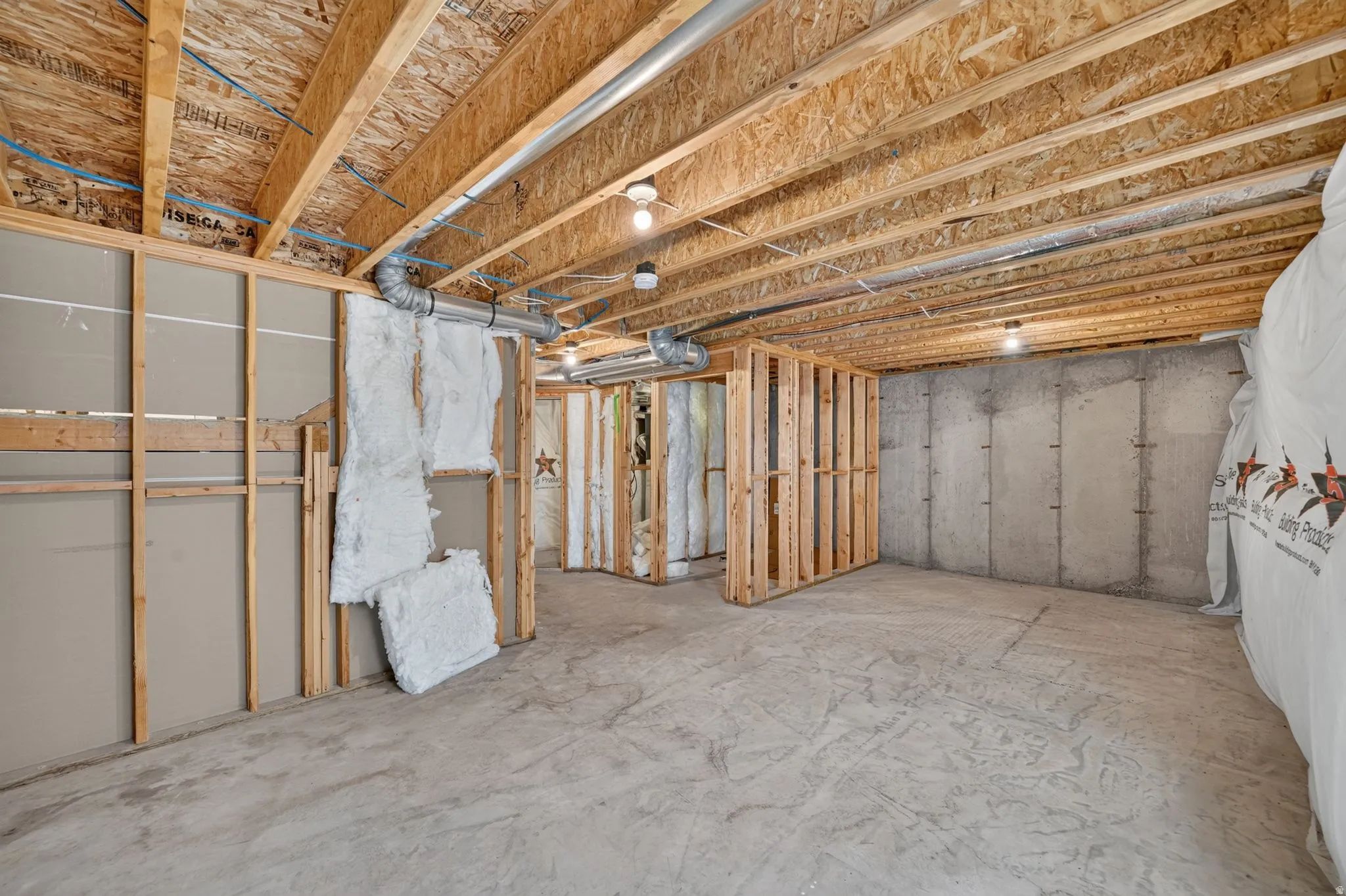 Unfinished basement featuring exposed wood joists, concrete flooring, concrete block walls, and partial wall framing with insulation