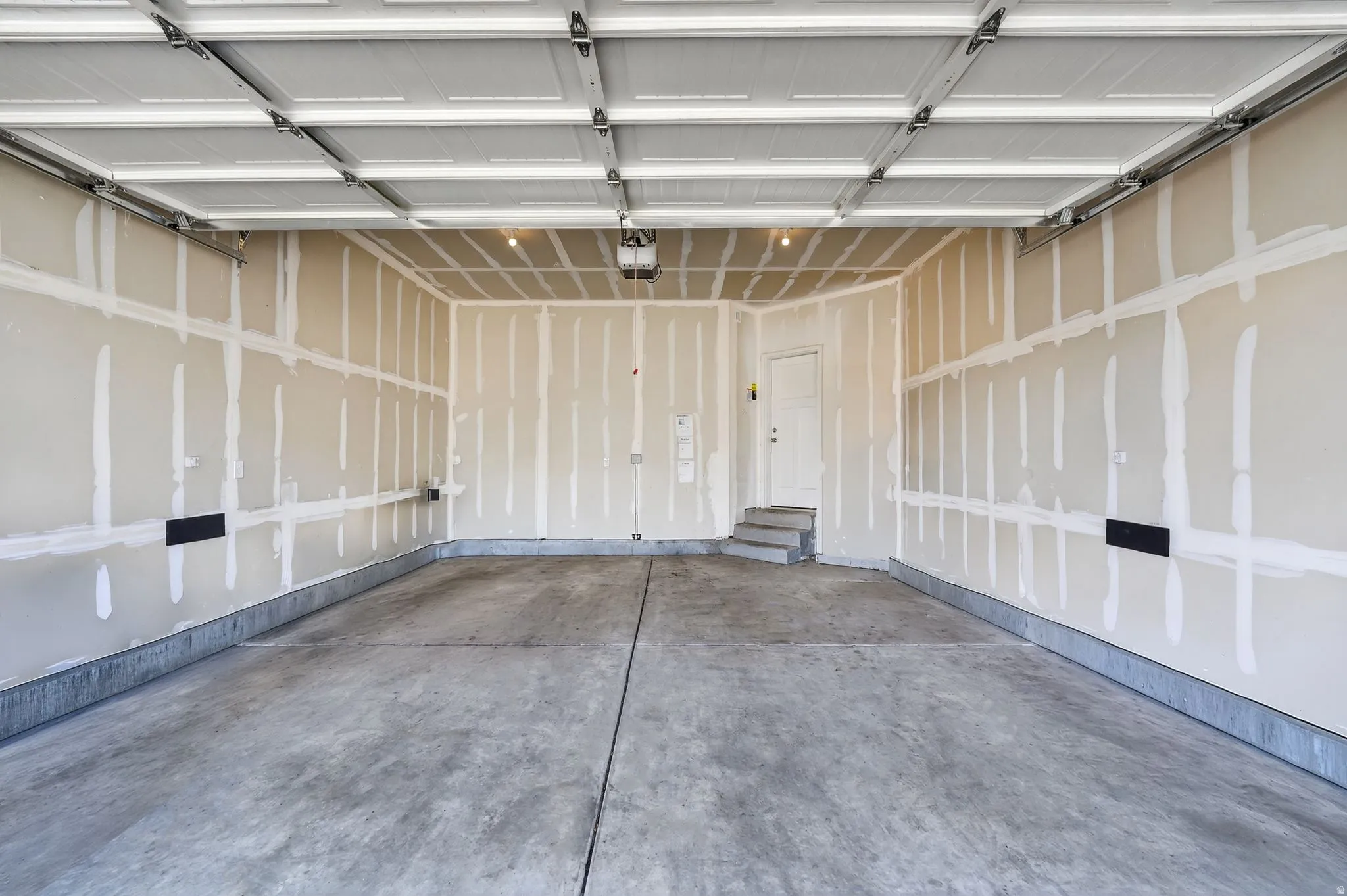 Spacious garage featuring a concrete floor, high ceiling, drywall-ready walls, and an interior access door with steps