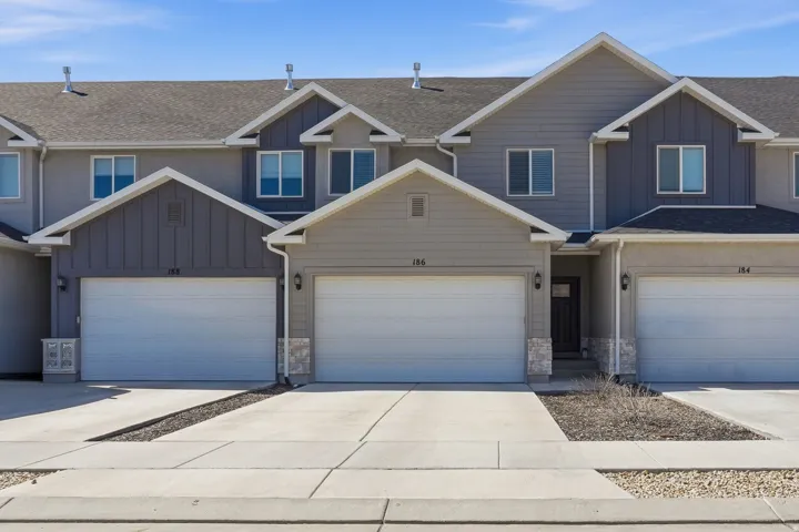 Modern townhome exterior featuring an attached garage, vertical siding accents, stone veneer details, and a covered entry