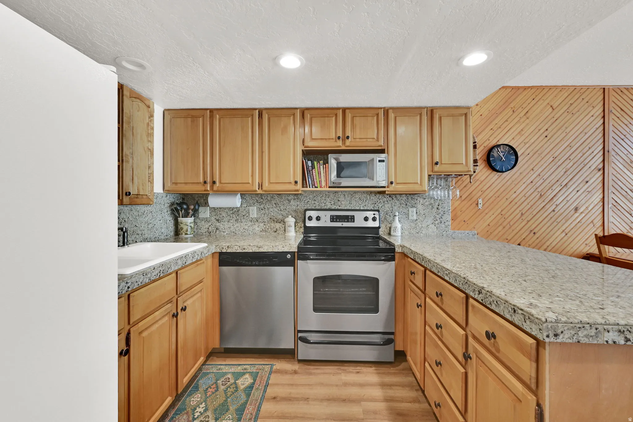 Kitchen featuring wood-finish cabinetry, light-toned granite countertops, and stainless steel appliances including a built-in microwave, dishwasher, and range