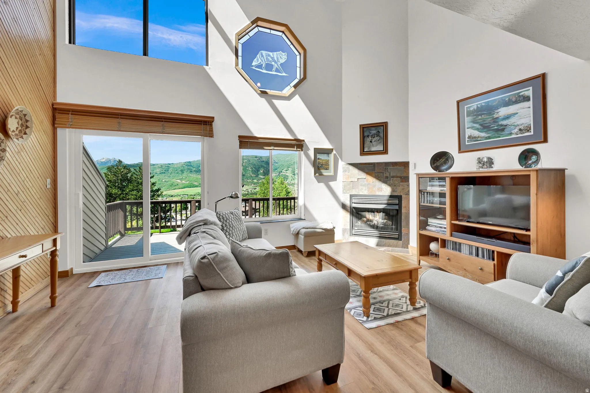 Vaulted ceiling living space featuring a stone fireplace, wood-finish flooring, and a sliding glass door opening to a private balcony
