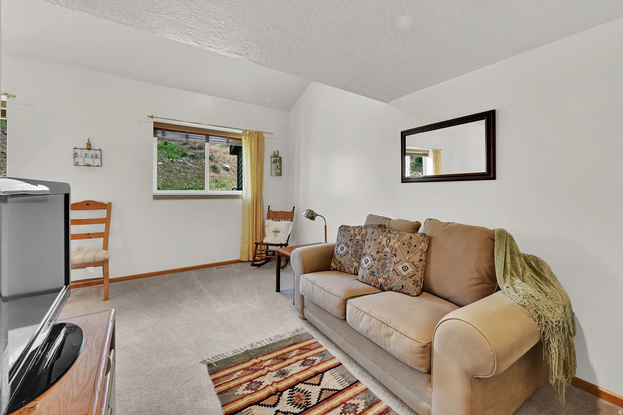 Bright living area featuring vaulted ceilings, light grey carpet flooring, white walls, and a window with exterior views