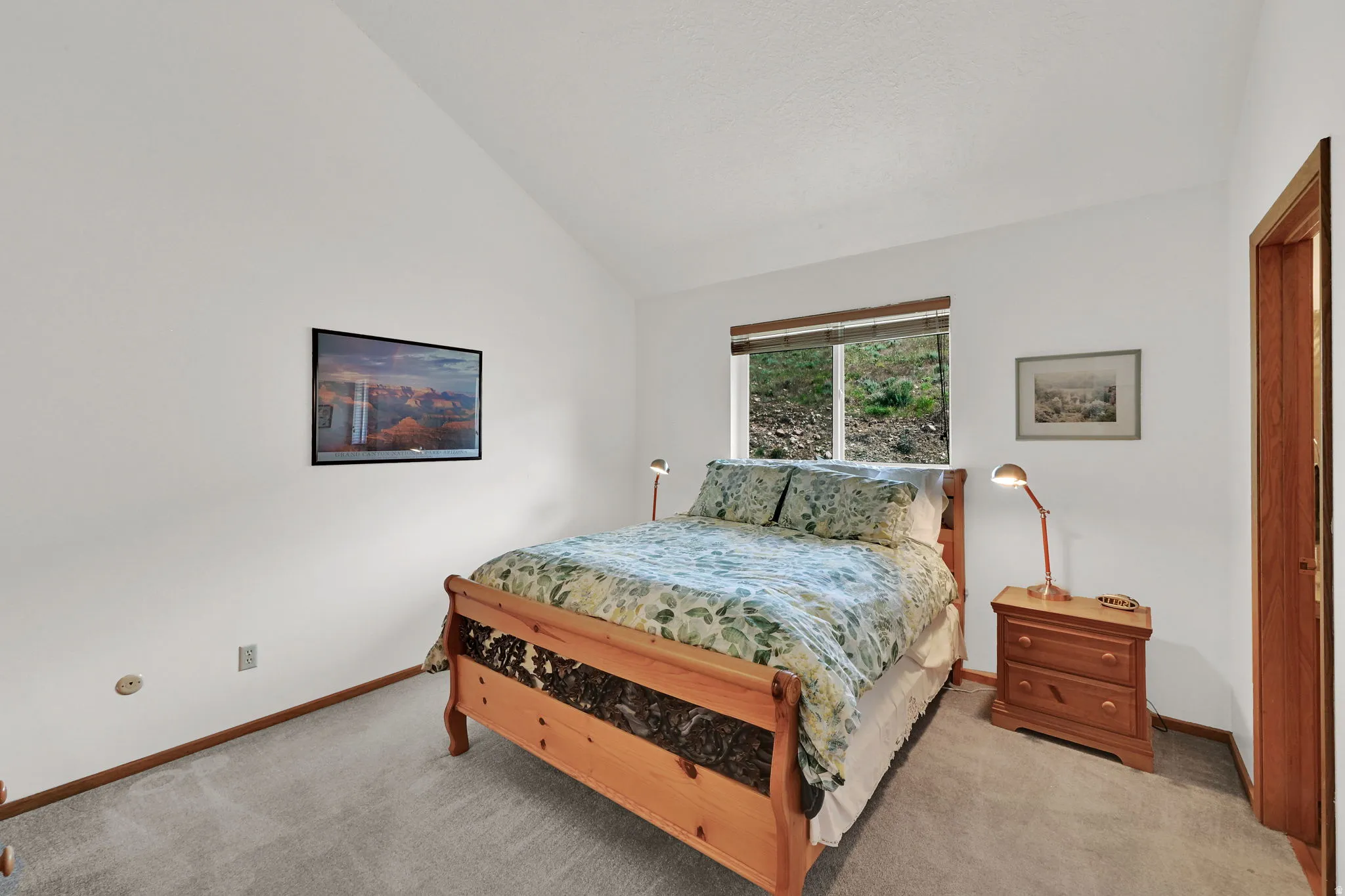 Primary Bedroom. Vaulted ceiling room with light gray carpet flooring, white painted walls, and wood trim