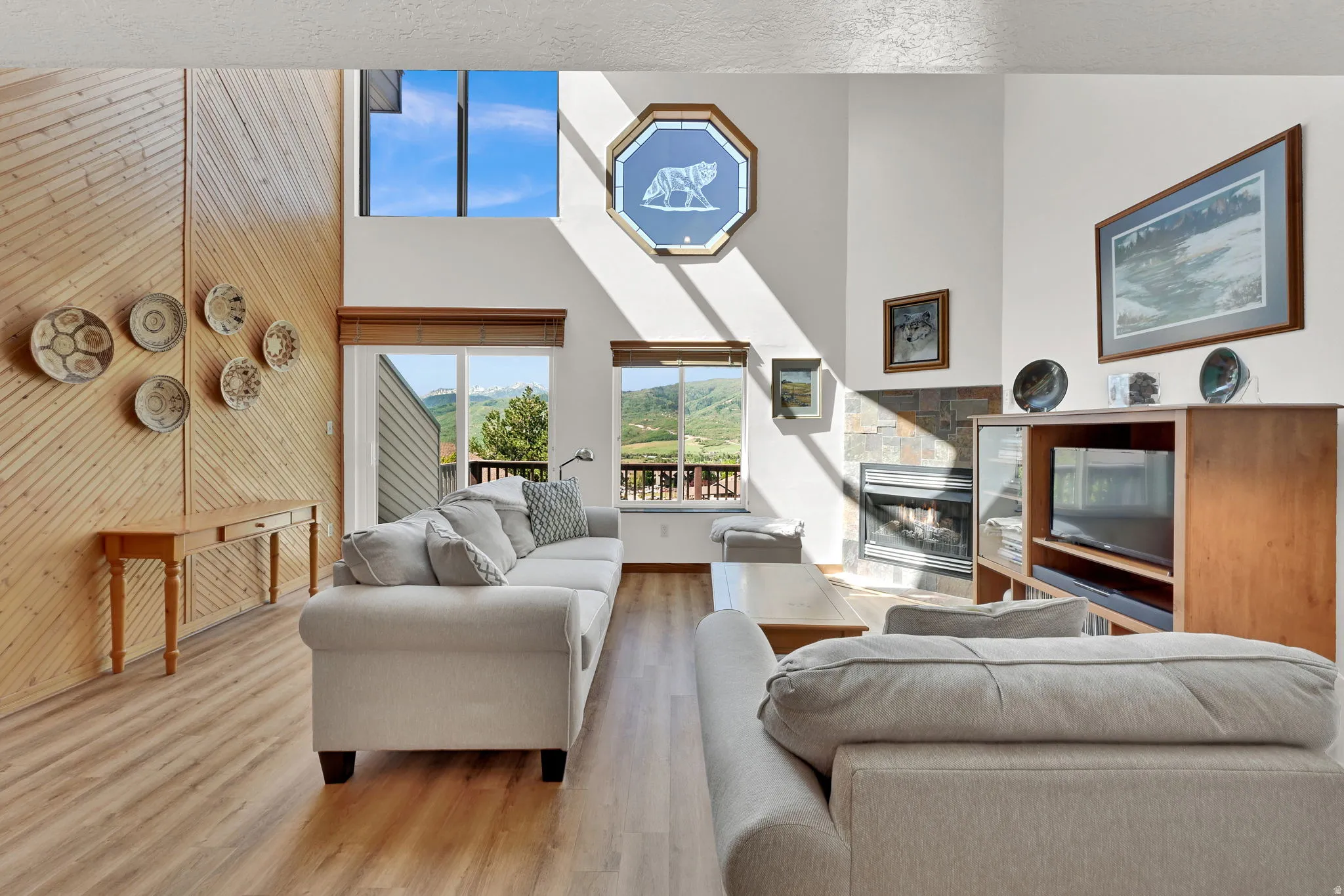 Vaulted living space featuring a floor-to-ceiling accent wall with horizontal wood paneling, wood-finish flooring, and a stone-faced fireplace
