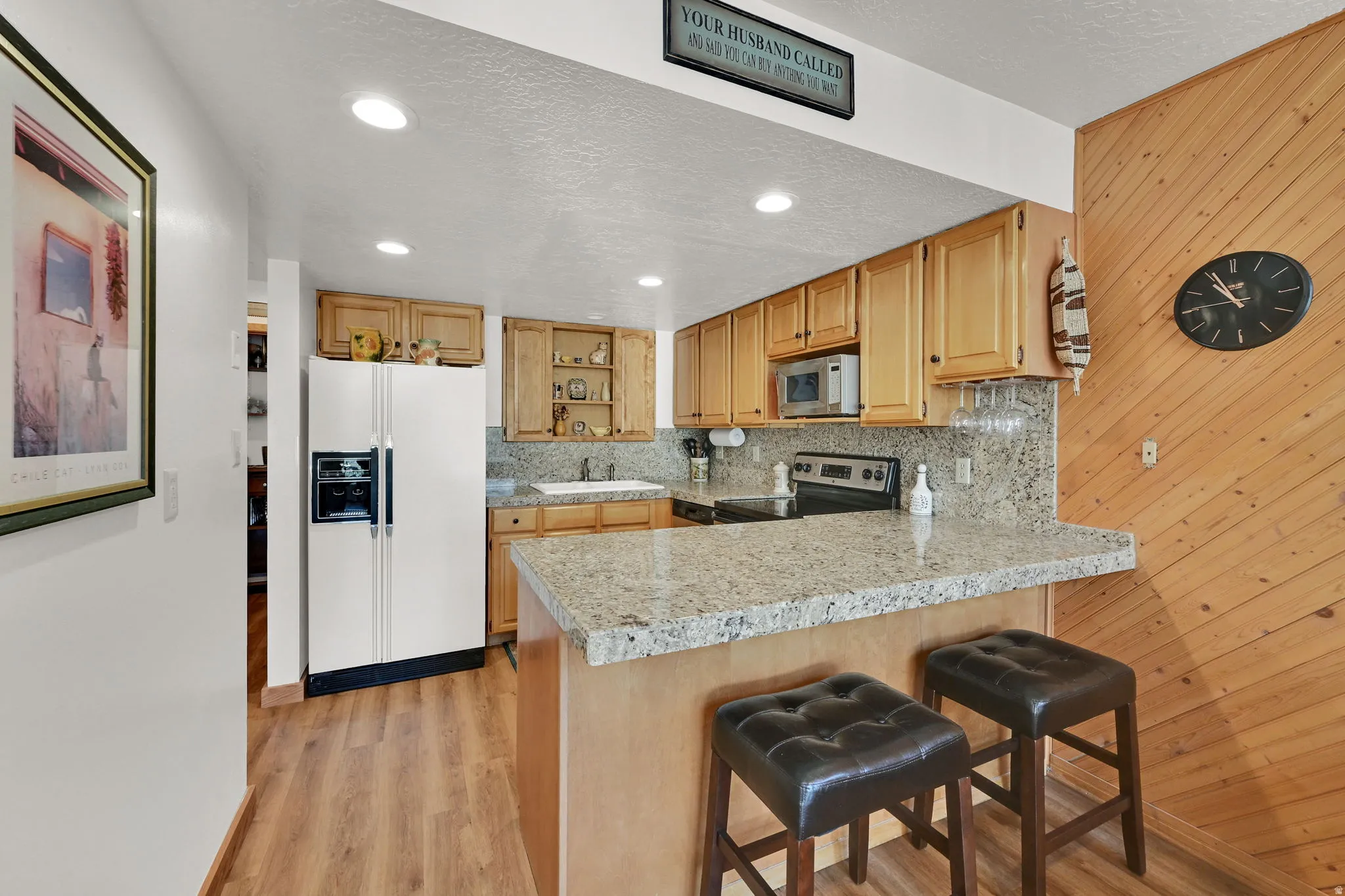 Kitchen featuring wood-finish flooring, light wood cabinetry, stone countertops, and a built-in breakfast bar