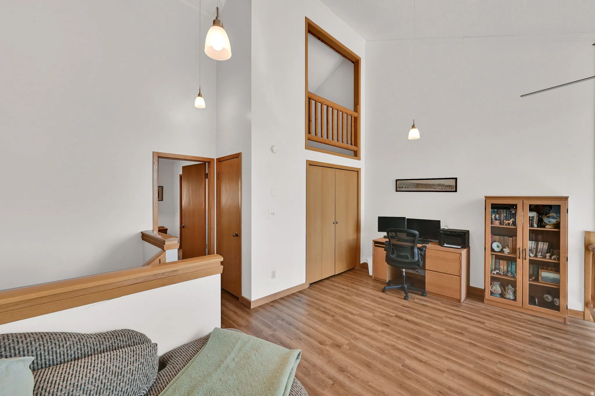 Vaulted ceilings featuring pendant lighting, wood-finish flooring, a built-in wood railing, and a windowed architectural element