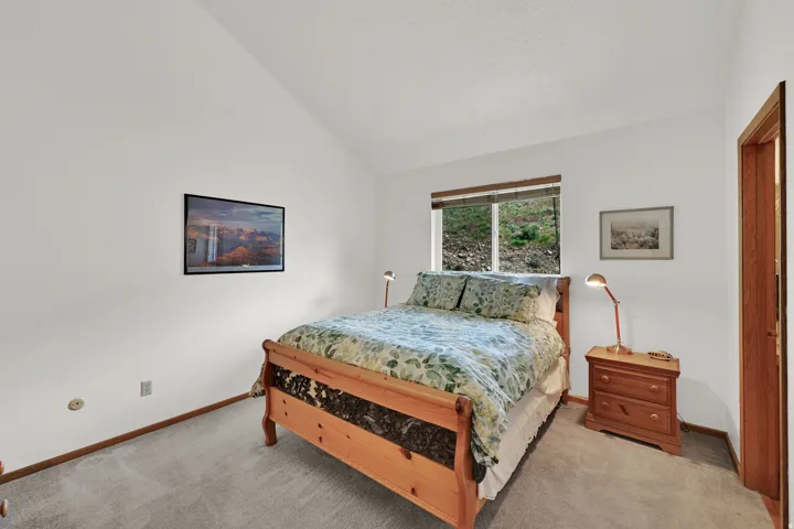 Primary Bedroom. Vaulted ceiling room with light gray carpet flooring, white painted walls, and wood trim