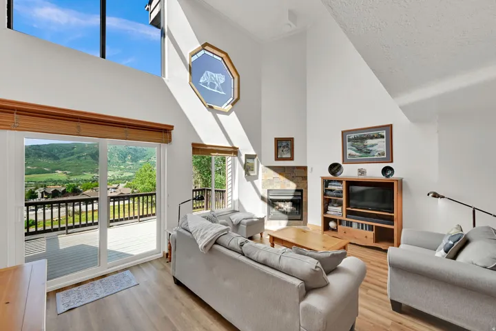 Vaulted living room featuring wood-finish flooring, a stone-surround fireplace, and a large sliding glass door opening to an outdoor deck