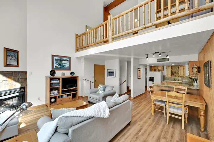 Open-concept living space featuring a high ceiling, a stone-faced fireplace, and wood-finish flooring