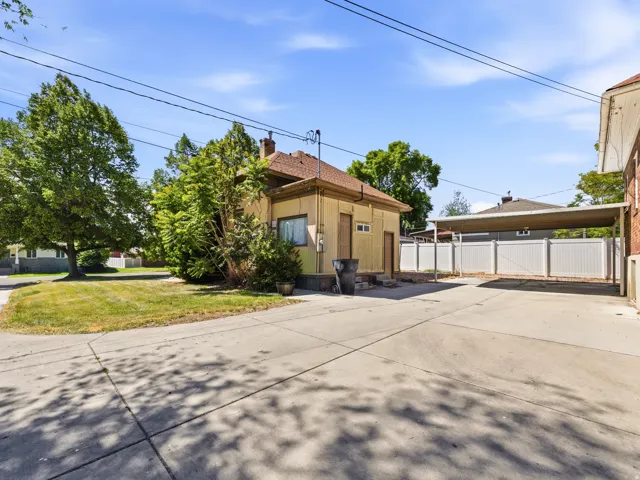 Concrete driveway with a covered carport, bordered by a white privacy fence