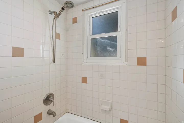 Bathtub and shower enclosure featuring white square tiles with occasional tan accent tiles