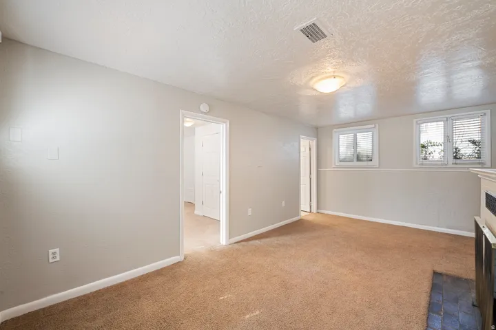 Carpeted room with light neutral walls, featuring two windows with horizontal blinds, a ceiling-mounted light fixture, and an entry doorway