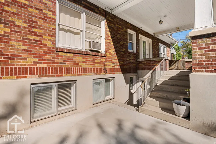 Brick exterior featuring a covered porch, concrete steps with metal handrails, and multiple windows