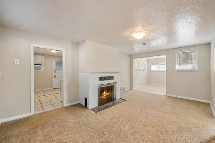Living area with a white brick fireplace featuring a metal grate, carpet flooring, and neutral wall paint