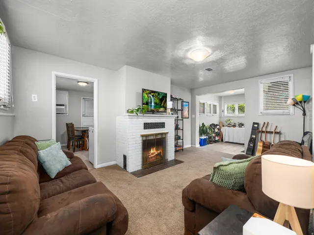 Living area featuring a white brick fireplace with a dark metal surround, textured ceiling, and neutral-toned carpeting