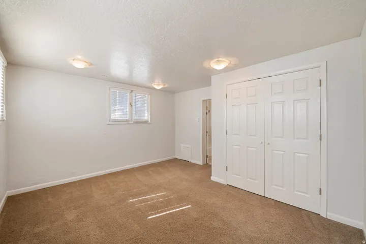 Carpeted room featuring white walls, two windows with blinds, a bi-fold closet with panel doors, and two flush mount ceiling lights