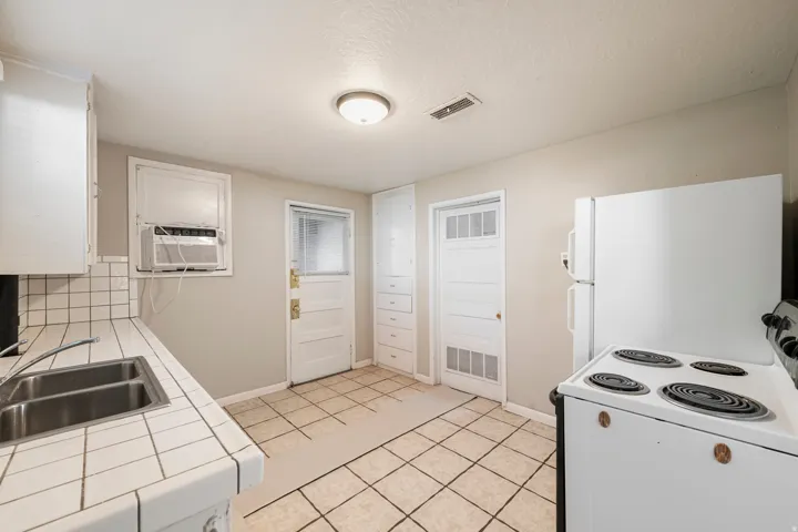 Kitchen featuring white cabinetry, tile countertops, a double basin stainless steel sink, and a freestanding electric range
