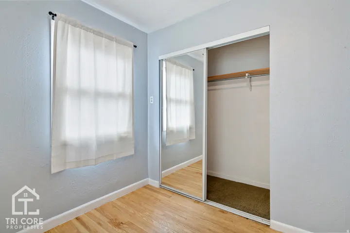 Bedroom featuring wood-finish flooring, light blue wall paint, a window with a white curtain, and a closet with mirrored sliding doors