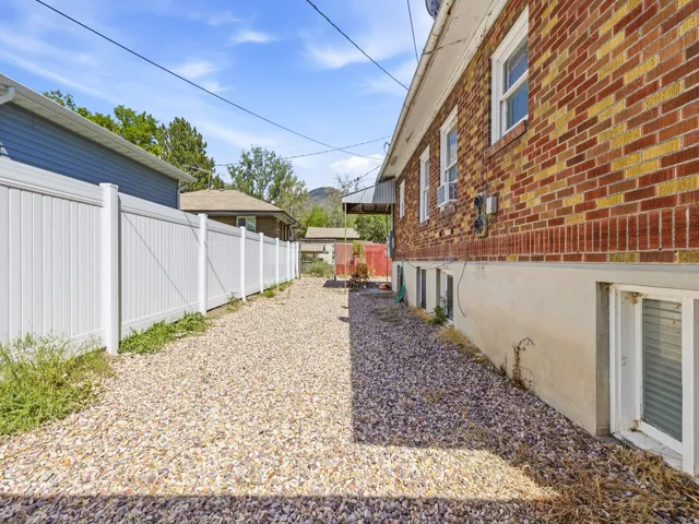 Gravel pathway bordered by a white privacy fence and a brick-sided exterior with multiple windows