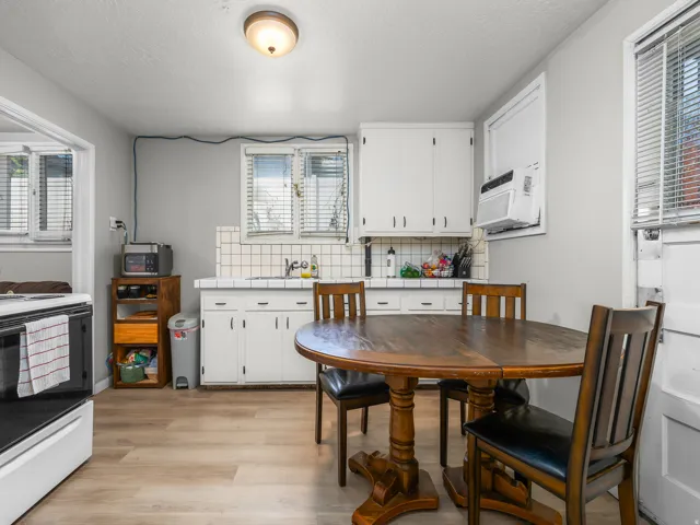 Kitchen featuring light wood-finish flooring, white cabinetry, a tiled backsplash, and a window-mounted air conditioning unit
