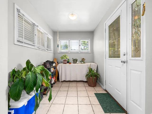 Enclosed entryway featuring ceramic tile flooring, multiple windows with blinds, a white entry door with decorative glass, and a matching sidelight