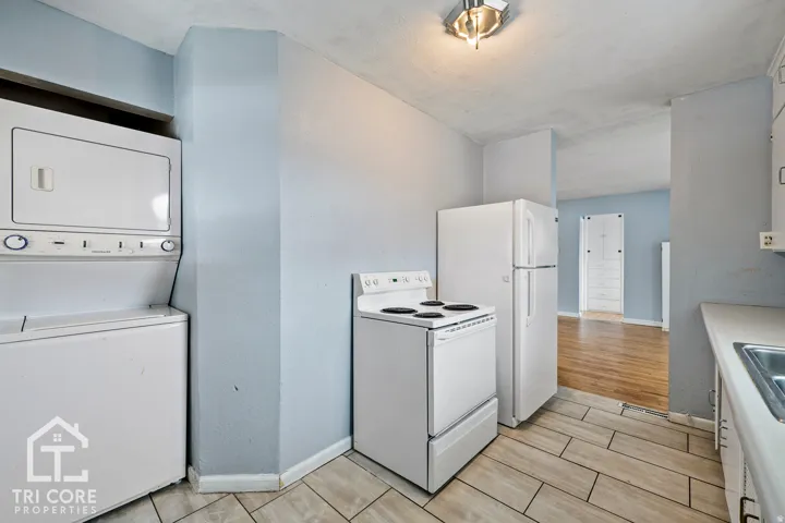 Kitchen area featuring white appliances, a stackable washer and dryer, tile flooring, and light blue walls