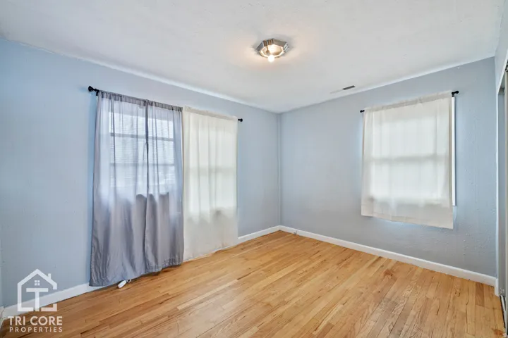 Bright room featuring wood flooring, neutral wall tones, two windows with window treatments, and a ceiling-mounted light fixture