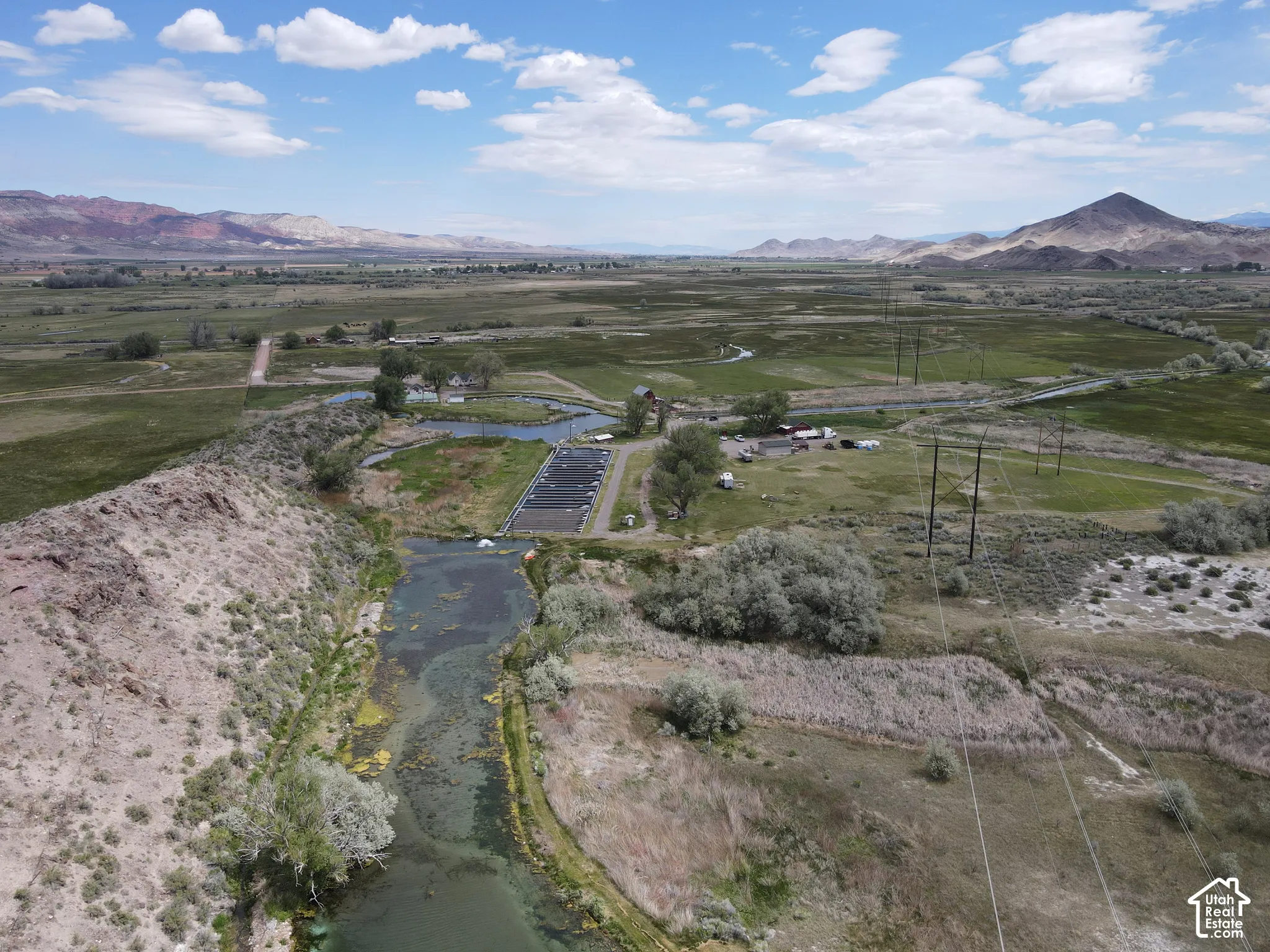 Expansive open terrain featuring a natural waterway, a small agricultural development, and distant mountains