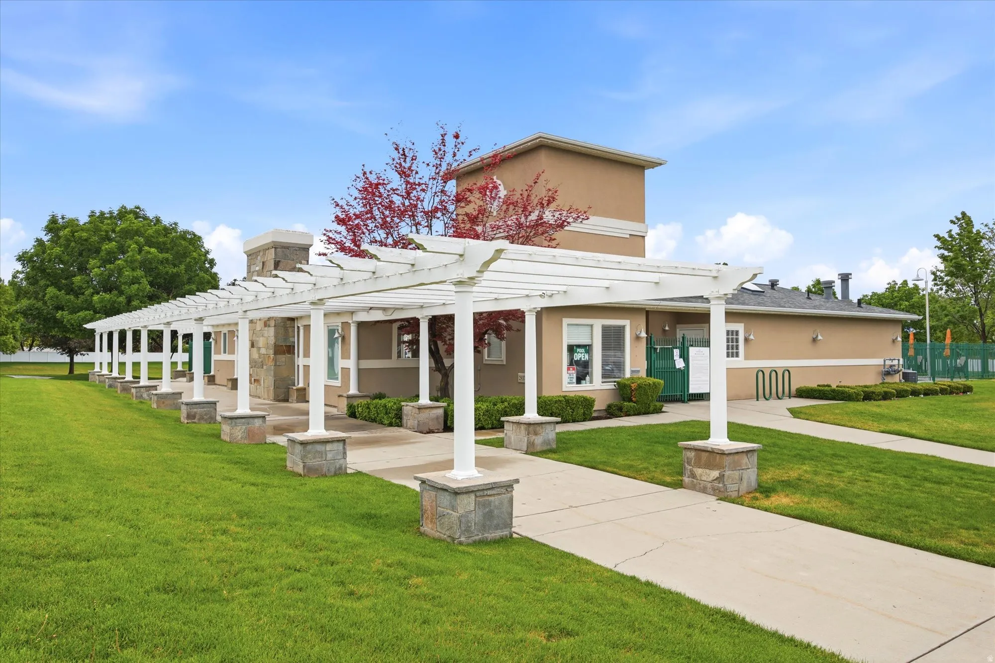 Exterior building featuring a pergola-covered walkway with stone bases, stucco siding, and a prominent stone chimney