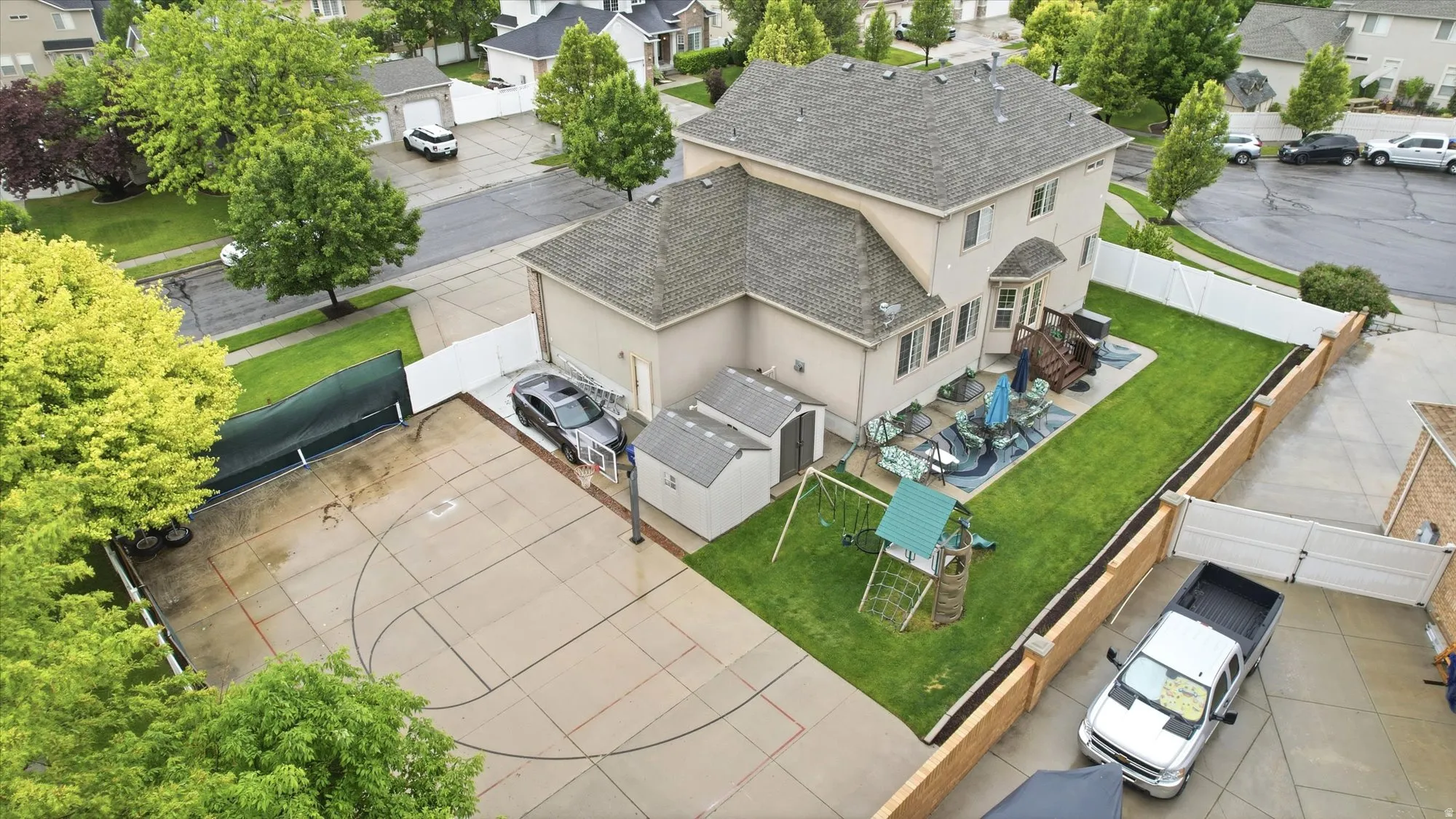 Spacious property featuring a large concrete sport court, a manicured lawn, a two-story residence with a patio, and a detached storage shed