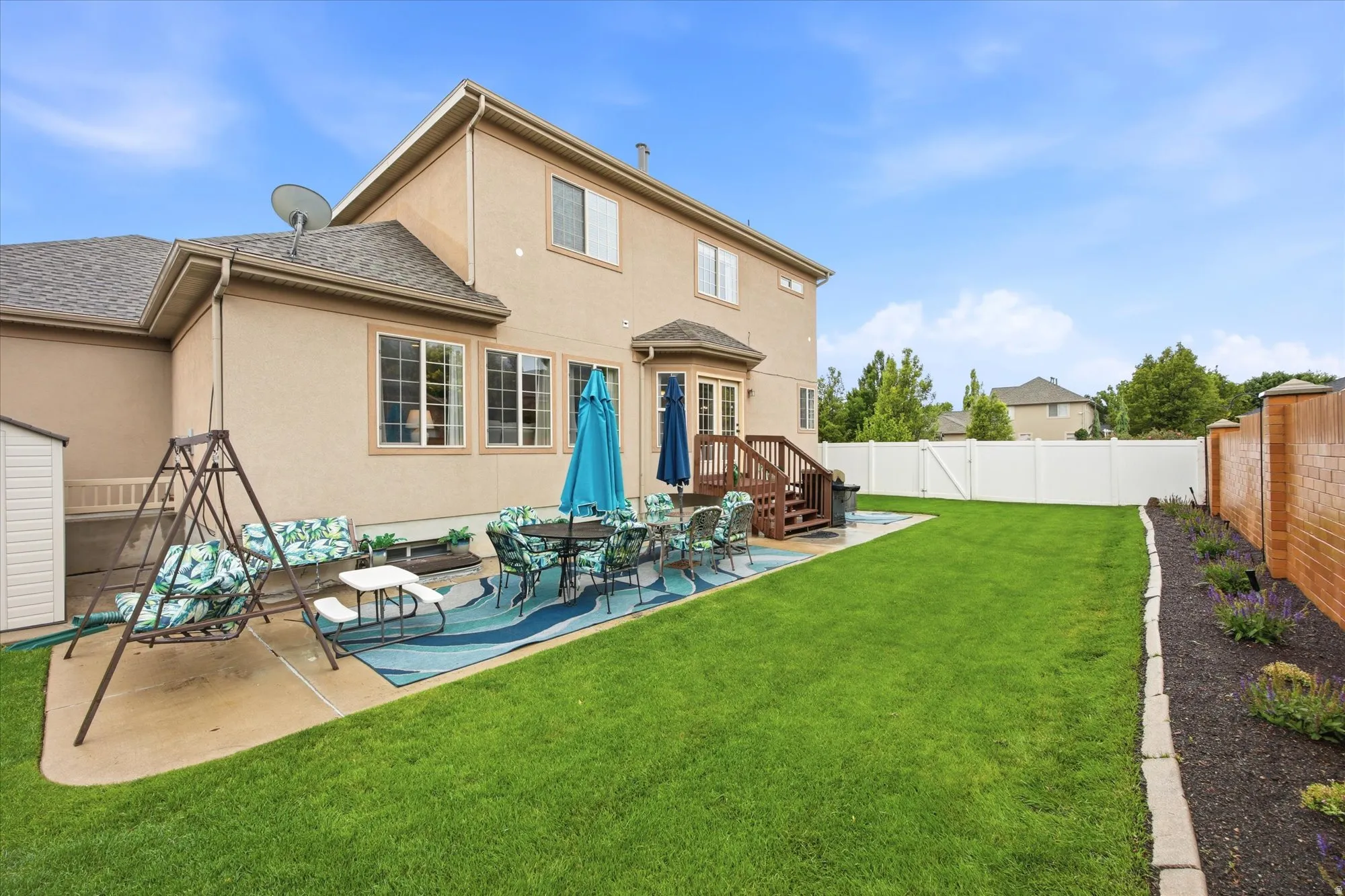 Spacious backyard featuring a manicured lawn, an expansive concrete patio, and a dedicated brick planter bed