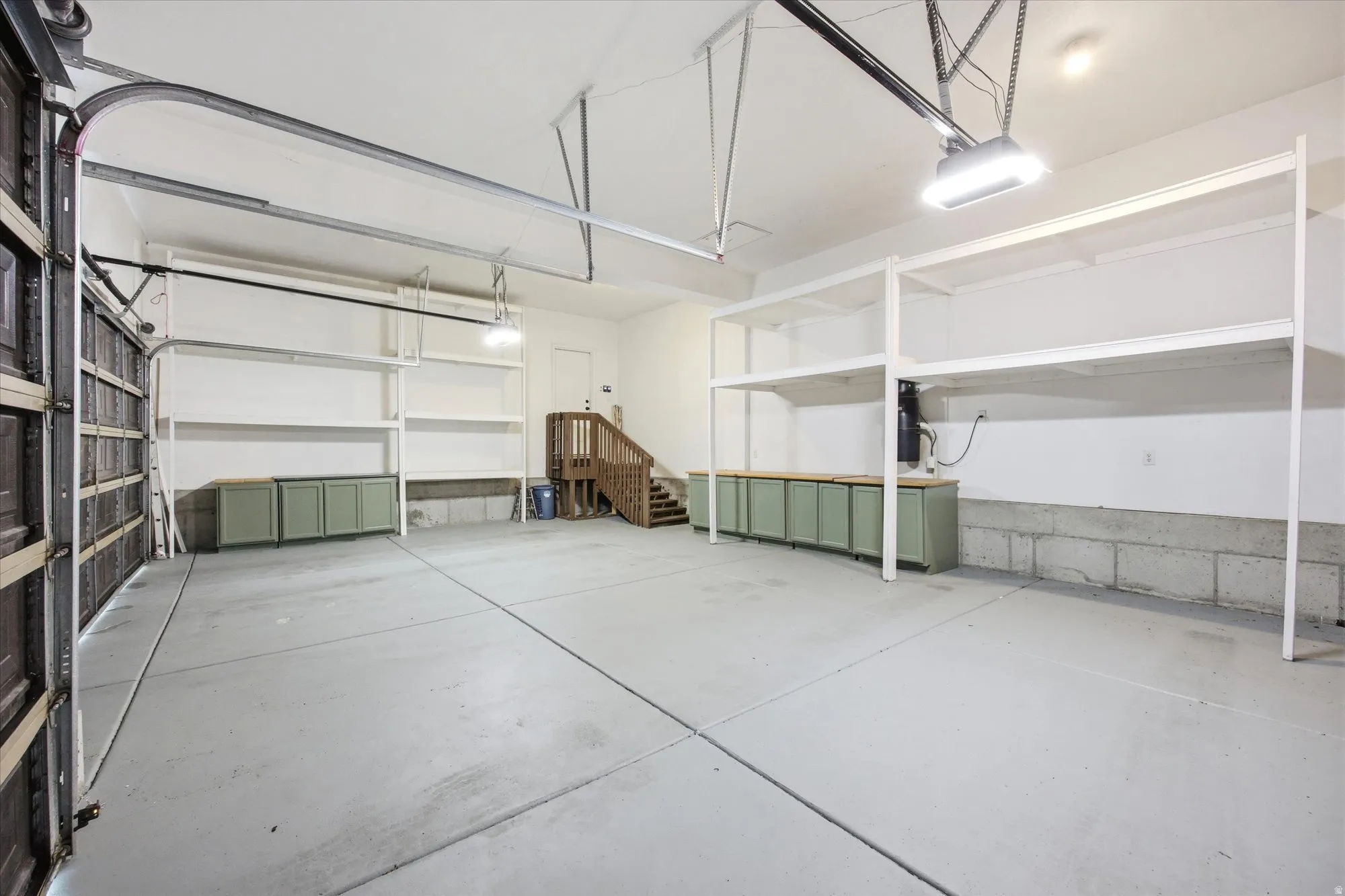 Spacious garage featuring concrete flooring, built-in shelving, two overhead garage door openers, and integrated cabinetry with countertops