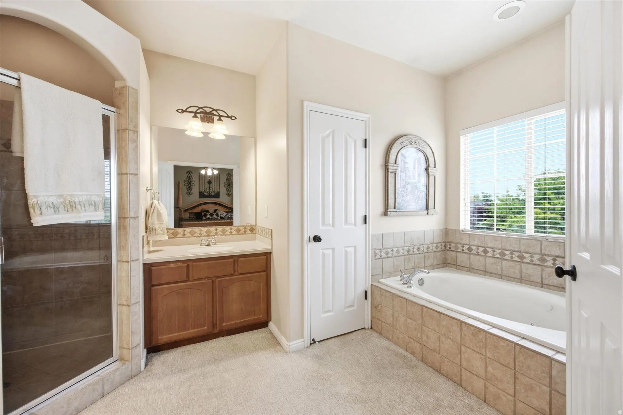 Bathroom featuring a built-in soaking tub, a separate glass-enclosed shower, a single vanity with wood cabinetry and a light-toned countertop, and a window with blinds