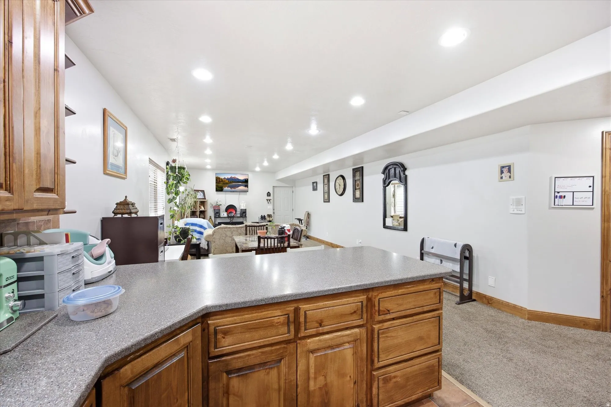 Spacious open-concept room featuring a functional peninsula with wood cabinetry and a stone-finish countertop, recessed lighting, and carpeted flooring in the living area