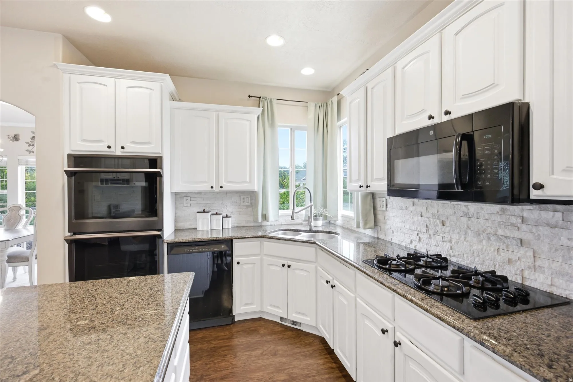 Modern kitchen featuring white cabinetry, a built-in double oven, a gas cooktop, stone countertops, and a stacked stone backsplash