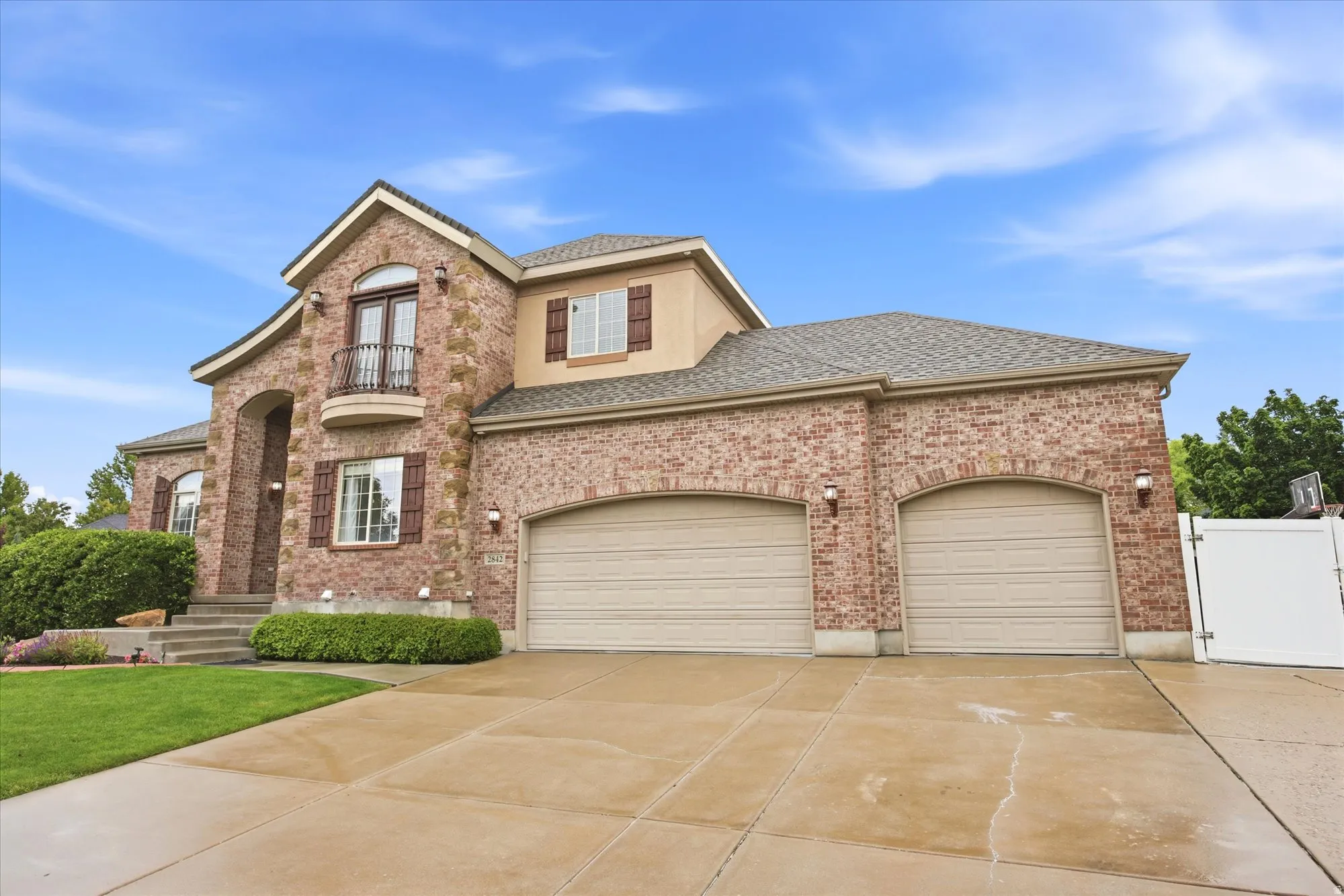 Brick and stucco exterior with a prominent arched entry, second-story balcony with iron railing, and a two-car garage with arched openings